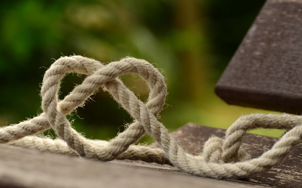 brown rope tangled and formed into heart shape on brown wooden rail connection